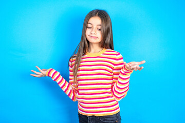 Careless attractive beautiful kid girl wearing  striped T-shirt shrugging shoulders, oops.