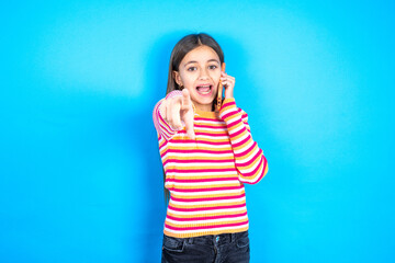 Positive beautiful kid girl wearing  striped T -shirt indicates directly at camera has telephone...