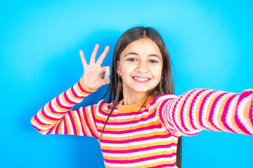 Portrait of pretty cheerful Young kid girl wearing striped t-shirt make selfie show okey symbol