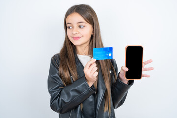 Young beautiful teen girl wearing biker jacket holding bank card modern device looking empty space