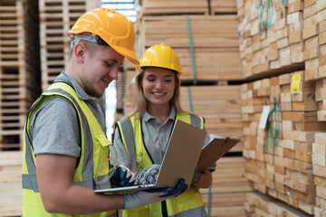 Male and female warehouse worker working with laptop computer in lumber storage warehouse. Workers working in timber storage warehouse. Manufacturing and warehouse concept