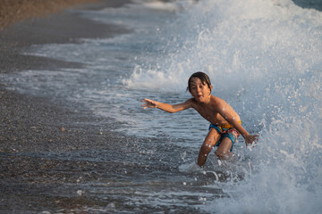 A boy running away from the waves on the beach.