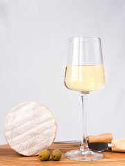A wineglass of white dry wine and camembert cheese on a wooden table. Close-up. Selective focus.