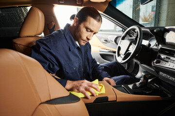 appealing devoted serviceman in blue uniform with collected hair cleaning car with yellow rag - obrazy, fototapety, plakaty