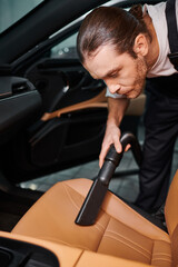 Obraz na płótnie Canvas good looking hard working serviceman in uniform using manual vacuum cleaner in car in garage