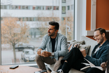Smiling mature businessman with coffee cup sitting by male colleague during conference meeting