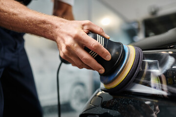 cropped view of dedicated hard working professional in uniform polishing car with special machine