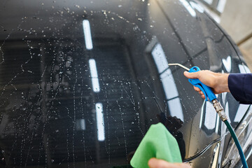 cropped view of hard working professional in uniform using water hose and rag to clean black car