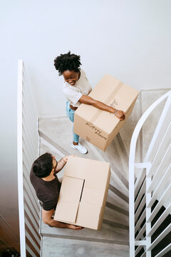 High angle view of multiracial couple carrying boxes while moving up on staircase at home