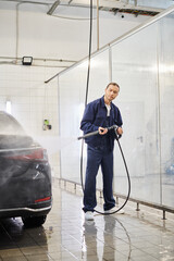 attractive hard working professional in blue uniform with collected hair using hose to wash car