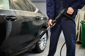 cropped view of devoted professional worker in blue comfy uniform preparing to use hose to wash car