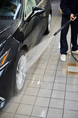 cropped view of dedicated professional worker in blue comfy uniform washing black car in garage