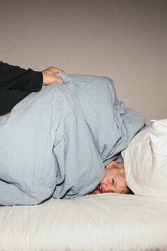 Cheerful boy hiding under blanket on bed at home