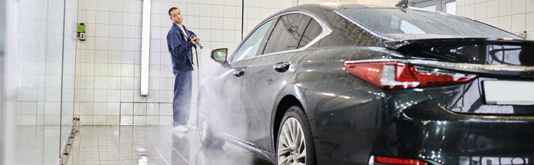 appealing devoted specialist in comfy blue uniform using hose to wash black modern car, banner