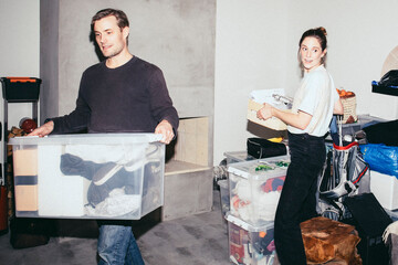 Man and woman helping each other while picking boxes during relocation of house