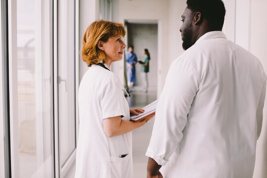 Senior female doctor discussing with male colleague in corridor at hospital
