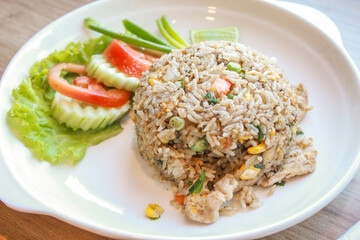 Pork fried rice served in a restaurant with wooden floor tables with tomatoes, cucumbers, scallions, fried rice, delicious food made from steamed rice.