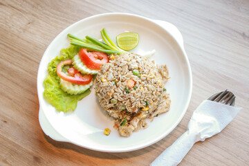 Pork fried rice served in a restaurant with wooden floor tables with tomatoes, cucumbers, scallions, fried rice, delicious food made from steamed rice.