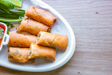 Freshly fried golden yellow spring rolls on a white plate with various vegetables and a delicious...