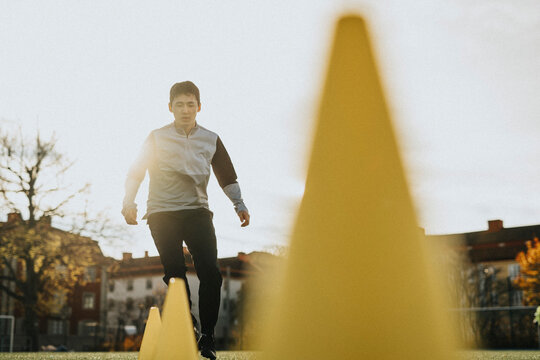 Determinant male athlete running amidst training cones at sports field