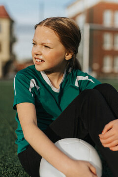 Elementary girl with soccer ball day dreaming while sitting at sports field