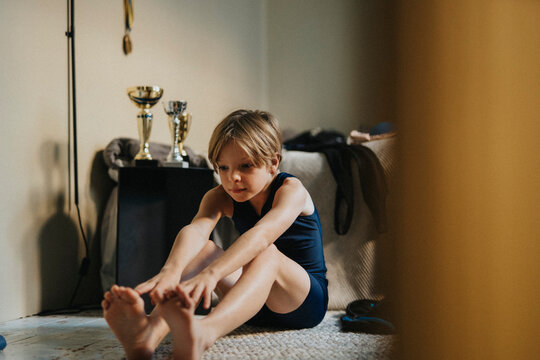 Elementary boy practices stretching exercise while sitting in bedroom