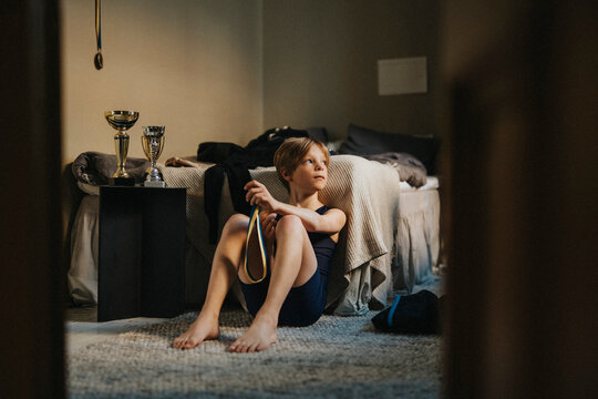 Contemplative elementary boy with medal sitting in bedroom at home - Powered by Adobe