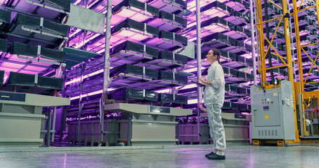 Young Female Farmer Standing in a Vertical Farm Facility with LED Lights. Hydroponics Technician...