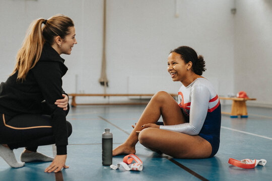 Happy teenage girl talking with female coach in school gymnasium