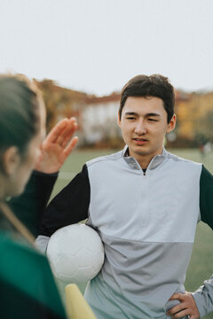 Female instructor explaining to male athlete while standing in sports field