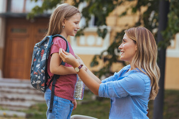 Happy family preparing for school. Little girl with mother. Mother saying goodbye to her daughter at school. Beginning of lessons. First day of fall.