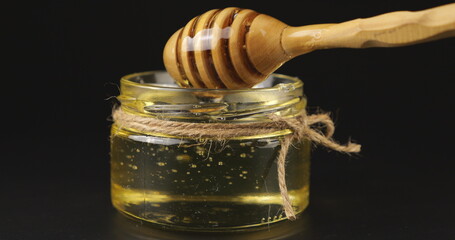 Honey flows down from a spoon spindle into a jar with honey on a black background.