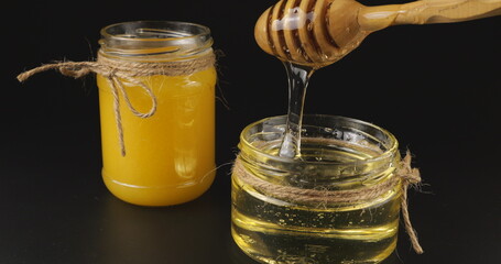 Honey flows down from a spoon spindle into a jar with honey on a black background.