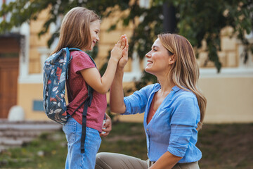Mother taking her daughter to school. Mother preparing her child for school in front of school....