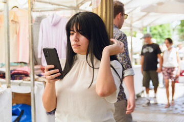 young latin woman tourist standing at fair using phone watching screen