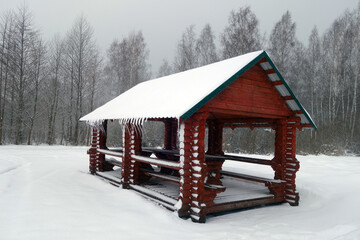 Wooden pavillion in snow with icicles on roof.