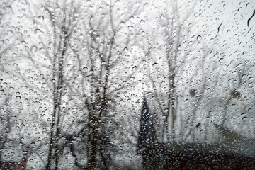 View on winter house and  trees through wet windshield with rain drops.