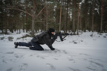 Fight scene in the forest in winter. A military man with a assault rifletakes a position a prone...