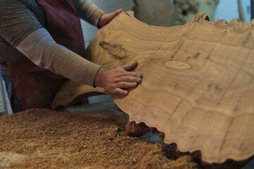 Hands carefully handle a uniquely shaped wooden slab, showcasing its organic curves. It's...