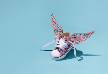 Baby sneaker, with pink details, decorated with a pair of wings, free active child creative concept.