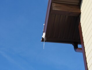 The edge of the roof with a little bit snow and icicles against the blue sky