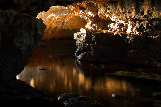Warm light filters into a tranquil cave pool, highlighting the textured rock surfaces and still water