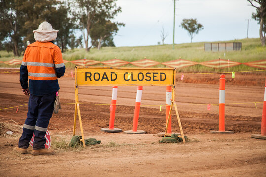 Bloke in hi-vis clothing standing beside road closed sign