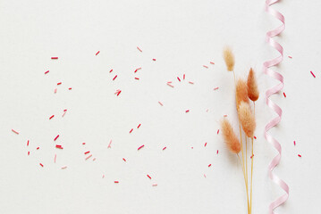 Dry flower branch, ribbon and candy sprinkles on a light gray background. Springtime, Easter,...