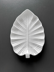 Empty white porcelain plate in shape of tree leaf and towel on dark gray background. View from above 