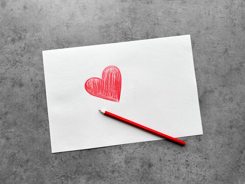 Hand drawn red heart on white paper with pencil next to it on gray background. Valentine's Day Mother's Day Children Charity Romantic Love Concept.