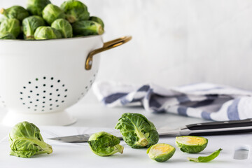 Fresh brussel sprouts on a cutting board with a colander full of them in behind.