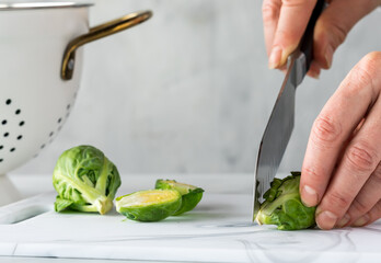 A close up of hands preparing fresh brussel sprouts for cooking. 