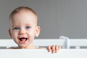 One year old baby standing in a crib smiling