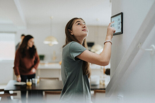 Girl adjusting room temperature through digital tablet mounted on wall at home